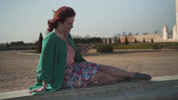 Мода залежних молода жінка в зеленому одязі, насолоджуючись сонцем біля фонтану перед палацом — стокове відео