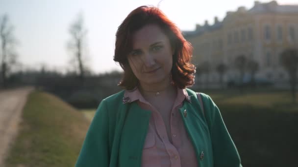 Young woman dancing in front of a palace and its canal under the sun wearing green fashion jacket and smiling — Stock Video