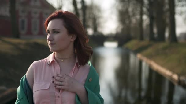 Jonge vrouw ontspannen in de buurt van een paleis deel kanaal tijdens een warme lente weer dragen van groene mode jas-Redhead — Stockvideo