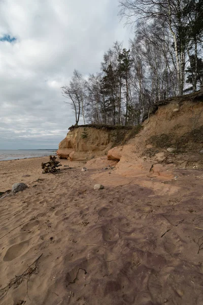 Limestone beach at the Baltic Sea with beautiful sand pattern and vivid red and orange color - Tourist writings on the walls and rocks and sand - Veczemju Klintis, Latvia - April 13, 2019