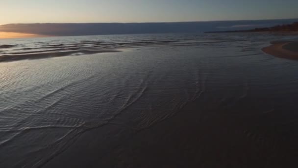 Puesta de sol carmesí con cielo claro y espejo como reflejos en el agua - Arena acanalada y olas - Tuja, Letonia - 13 de abril de 2019 — Vídeo de stock