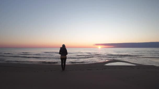 Молодая женщина, идущая вдоль пляжа, глядя на закат и морскую воду - Туя, Латвия - 13 апреля 2019 года — стоковое видео