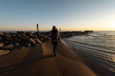 Baltık Denizi yakınlarındaki bir kaya plajında soğuk bir bahar günbatımının tadını çıkaran bir kadın.