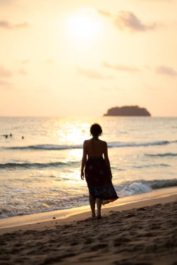 Bir gün batımı sırasında göndermek güzel beyaz ile Tayland Ko Chang plajda yürüyen renkli bir yaz elbise güzel kadın