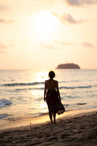 Bir gün batımı sırasında göndermek güzel beyaz ile Tayland Ko Chang plajda yürüyen renkli bir yaz elbise güzel kadın