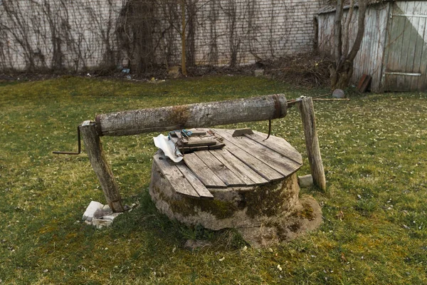 Piccolo vecchio pozzo in legno su erba vicino a una casa mannara in legno — Foto Stock