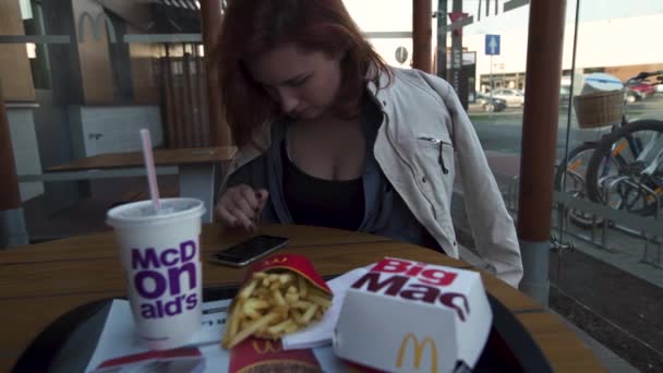 RIGA, LATVIA - 22 DE ABRIL DE 2019: Mujer joven usando su iPhone mientras come en Fast Food Restaurant Mcdonalds - Big Mac, papas fritas medianas y Coca-Cola — Vídeos de Stock