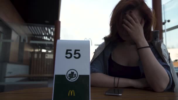 RIGA, LATVIA - 22 de abril de 2019: Esperando por ordem e pensando em seu peso - Jovem mulher comendo no restaurante Fast Food Mcdonalds — Vídeo de Stock