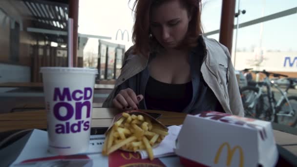 Riga, Lettország-április 22, 2019: fiatal nő használ vele iPhone evés közben a Fast Food Restaurant McDonalds-Big Mac, közepes krumpli és a Coca-Cola — Stock videók