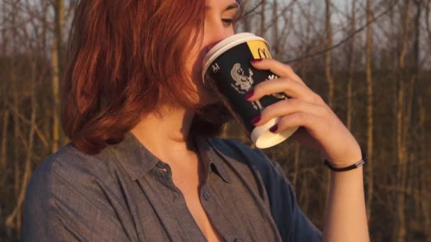 MARUPE, LATVIA - 22 DE ABRIL DE 2019: Mujer joven bebiendo café McDonalds al aire libre en un campo durante la puesta del sol — Vídeo de stock