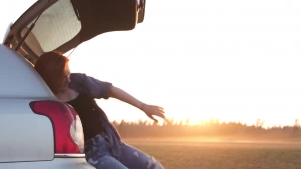 Jovem mulher bonita feliz e dançando em um tronco de carros durante uma viagem de carro na Europa nos últimos minutos do pôr do sol Golden Hour — Vídeo de Stock
