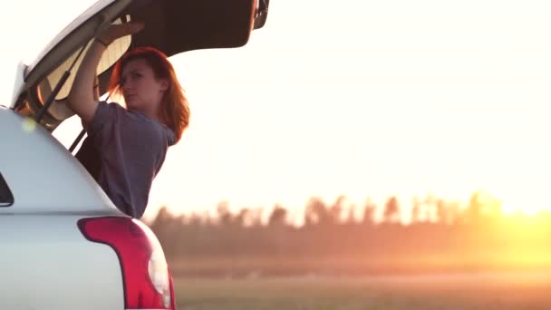 Mooie jonge vrouw blij en dansen in een auto kofferbak tijdens een Road Trip in Europa in de laatste minuten van Golden Hour Sunset — Stockvideo