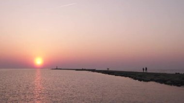 Ufuk ve berrak gökyüzüne yakın büyük bir güneş ile gün batımının son dakikasında deniz feneri