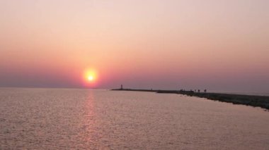 Ufuk ve berrak gökyüzüne yakın büyük bir güneş ile gün batımının son dakikasında deniz feneri