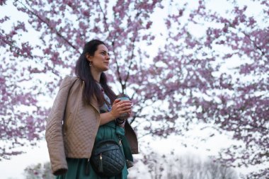 Zümrüt rengi etek giyen genç bir kadın Riga, Doğu Avrupa 'nın başkenti Letonya' da bir parkta renkli sakura kirazı çiçeği içiyor.
