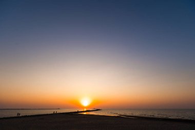 Ufuk ve berrak gökyüzüne yakın büyük bir güneş ile gün batımının son dakikasında deniz feneri