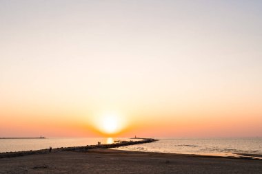 Ufuk ve berrak gökyüzüne yakın büyük bir güneş ile gün batımının son dakikasında deniz feneri