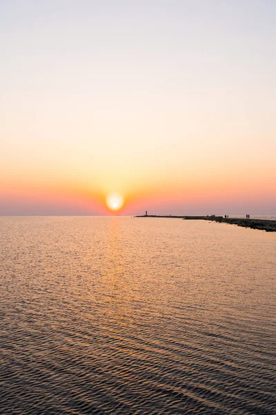 Ufuk ve berrak gökyüzüne yakın büyük bir güneş ile gün batımının son dakikasında deniz feneri — Stok fotoğraf