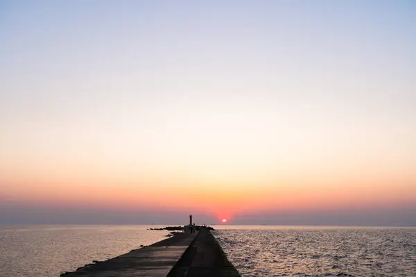 Ufuk ve berrak gökyüzüne yakın büyük bir güneş ile gün batımının son dakikasında deniz feneri — Stok fotoğraf