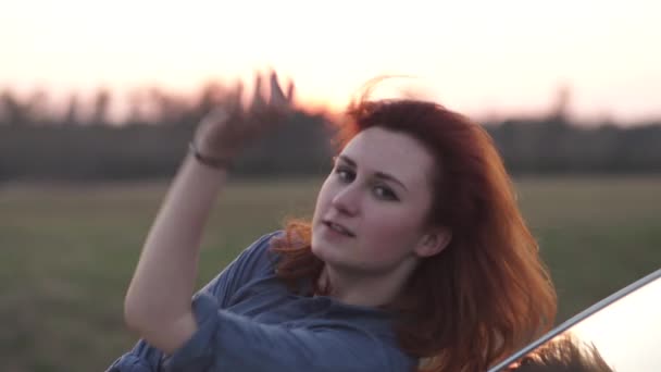 Close up de dança jovem ruiva jaqueta jeans azul durante um pôr do sol perto de um carro — Vídeo de Stock