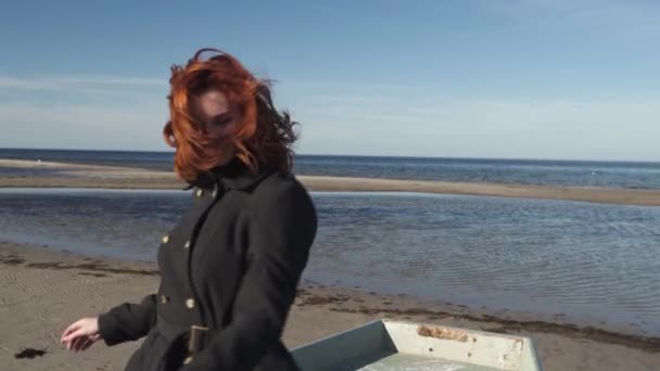 Молода жінка, що сидить у човні на пляжі в сонячну погоду на Балтійському морі, танцює і заповнює глупоту — стокове відео