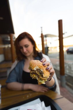 Hamburger yakın - Fast Food Restaurant'ta yemek yiyen Genç Kadın - Cheeseburger, orta boy patates kızartması ve soda