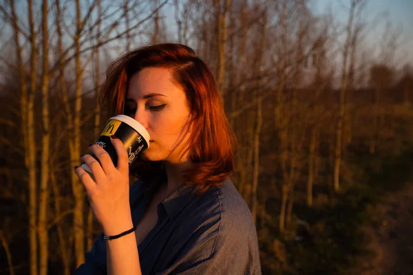 MARUPE, LATVIA - APRIL 22, 2019: Young woman drinking McDonalds coffee outdoors in a field during sunset — Stock Photo, Image