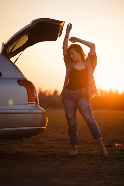 Szép fiatal nő boldog és táncolt egy autó törzs során közúti utazás Európában az utolsó percben a Golden Hour naplemente — Stock Fotó