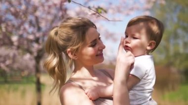 Genç anne düşen pembe yaprakları ve güzel çiçekleri ile çiçek açan Sakura Kiraz ağaçları altında onu küçük bebek erkek çocuk çocuk tutan