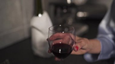 Bekar kadın mavi sabah elbisesi giyen bir mutfakta bir bardak kırmızı şarap içme - Gülerek ve gülümseyerek
