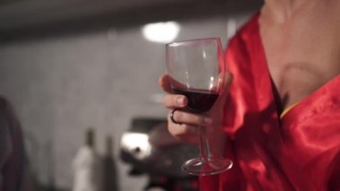 Mutfakta sohbet eden ve camdan kırmızı şarap içen iki kadın - Biri mavi sabah elbisesi, diğer kırmızı bornoz elbisesi - Gülerek ve gülümseyerek