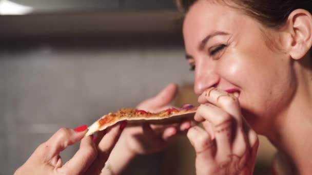 Две девушки женщины едят пиццу и наслаждаются вечерним разговором перед выходом - одна в синем утреннем платье, другая в красном халате - смеются и улыбаются — стоковое видео
