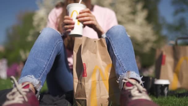 里加，拉脱维亚 - 2019年4月28日：成功的女商人吃麦当劳巨无霸汉堡和喝可口可乐享受她的休闲空闲时间在公园 — 图库视频影像
