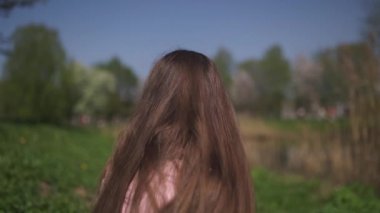 Yavaş Hareket 120fps: Genç mutlu gezgin kahverengi saçlı kadın kız gülümseyen ve Baltık eyaletlerinde pembe bir sakura kiraz çiçeği ağaçları ile yeni bir hedef ülkede etrafında dönüyor - Uçan saç
