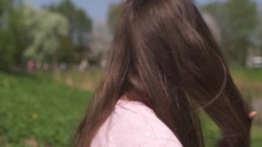 Yavaş Hareket 120fps: Genç mutlu gezgin kahverengi saçlı kadın kız gülümseyen ve Baltık eyaletlerinde pembe bir sakura kiraz çiçeği ağaçları ile yeni bir hedef ülkede etrafında dönüyor - Uçan saç