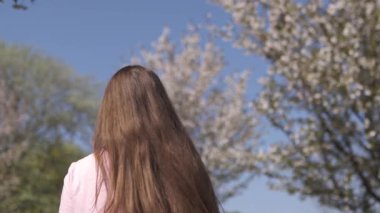 Yavaş Hareket 120fps: Genç mutlu gezgin kahverengi saçlı kadın kız gülümseyen ve Baltık eyaletlerinde pembe bir sakura kiraz çiçeği ağaçları ile yeni bir hedef ülkede etrafında dönüyor - Uçan saç