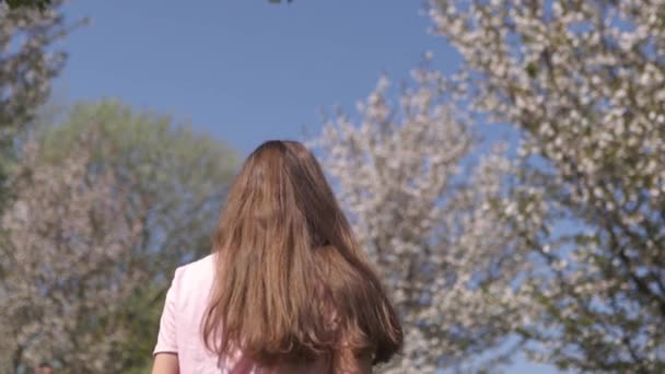 Zeitlupe 120fps: junge, glückliche Frau mit braunhaarigen Haaren lächelt und dreht sich um in einem neuen Zielland mit rosa Sakura-Kirschblütenbäumen in den baltischen Staaten - fliegendes Haar — Stockvideo