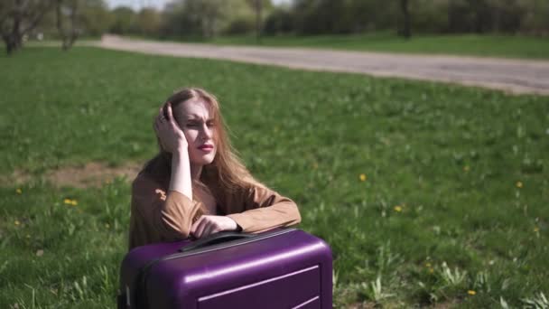 Traurige Reisende verpassten Flug und Bus - auf ihrem Koffer sitzend und weinend - Gefühle einer weißen kaukasischen Frau mit hellem langen Haar, BH und beiger Jacke — Stockvideo