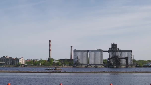 Říční člun se rozjede podél řeky Daugava s escavátorem na palubě-slunečné počasí s přístavem na pozadí — Stock video