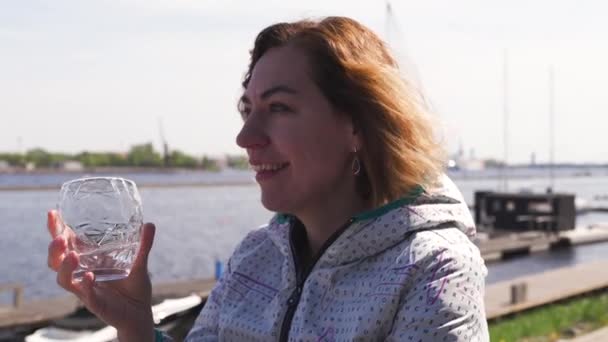 Feliz viajero bebiendo agua en un restaurante - Cabello castaño ondulado, mujer blanca caucásica usando chaqueta ligera en primavera soleado — Vídeo de stock