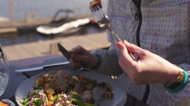 Feliz viajero comiendo plato de costillas en un restaurante pelo castaño ondulado, mujer blanca caucásica usando chaqueta ligera en primavera soleado — Vídeo de stock