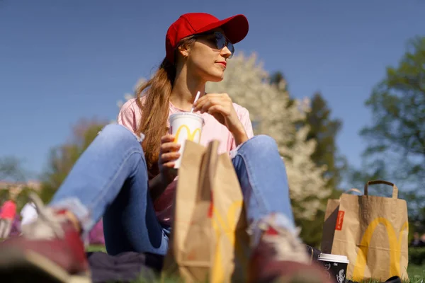 Рига, Латвія-28 квітня 2019: успішна Ділова жінка їсть МакДональдз Big Mac бургер Сирота і Питна Coca Cola користується її дозвілля вільний час в парку — стокове фото