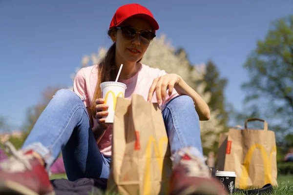 Рига, Латвія-28 квітня 2019: успішна Ділова жінка їсть МакДональдз Big Mac бургер Сирота і Питна Coca Cola користується її дозвілля вільний час в парку — стокове фото