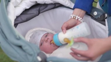 Anne parlak mavi meme ile plastik bir şişeden bebek bebek çocuk sütü besler - Beyaz beyaz çocuk bir anne el görünür - Beyaz çarşaf ile bir bebek arabası döşeme