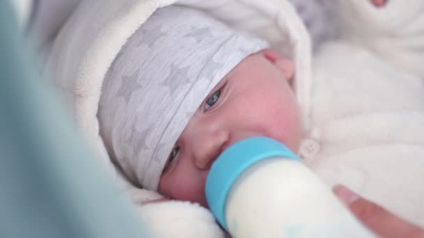 Mutter füttert Säugling Säuglingsmilch aus Plastikflasche mit leuchtend blauer Brustwarze - kaukasisches weißes Kind mit sichtbarer Hand der Eltern - liegt im Kinderwagen mit weißen Laken — Stockvideo