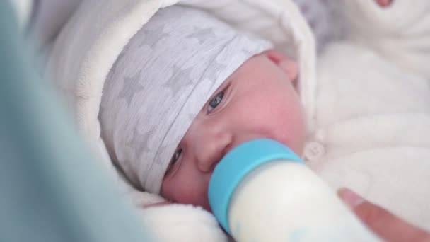 Madre alimenta a bebé niño niño leche de un biberón de plástico con un pezón azul brillante - Niño blanco caucásico con una mano de los padres visible - Colocación en un carro de bebé con sábanas blancas — Vídeo de stock