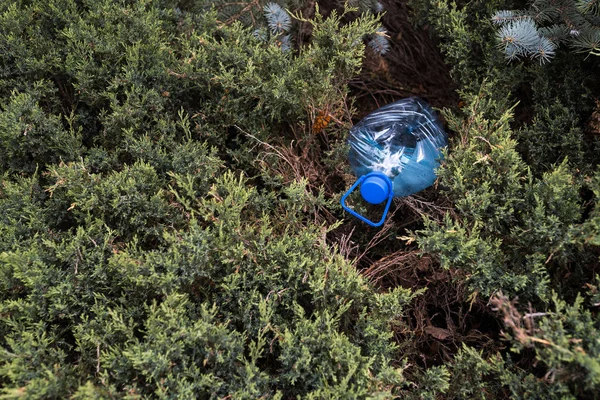 Blue big plastic bottle lying on the ground in tree in a park forest - Thrown out not recycled - Trash and pollution of the city and nature - Decayed rubbish