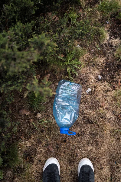 Man found standing feet - Blue big plastic bottle lying on the ground in tree in a park forest - Thrown out not recycled - Trash and pollution of the city and nature - Decayed rubbish