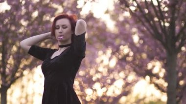 Mutlu genç seyahat dansçı kadın portresi bir sakura kiraz çiçeği parkta serbest zaman zevk - Kafkas beyaz kızıl kız - Giyinmiş siyah chocker, siyah elbise ve siyah golf