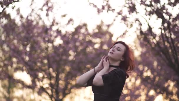 Портрет счастливой молодой танцовщицы, наслаждающейся свободным временем в парке цветения сакуры - белой белой белой рыжей девушки - одетой черной шоколадкой, черным платьем и черными гольфами — стоковое видео